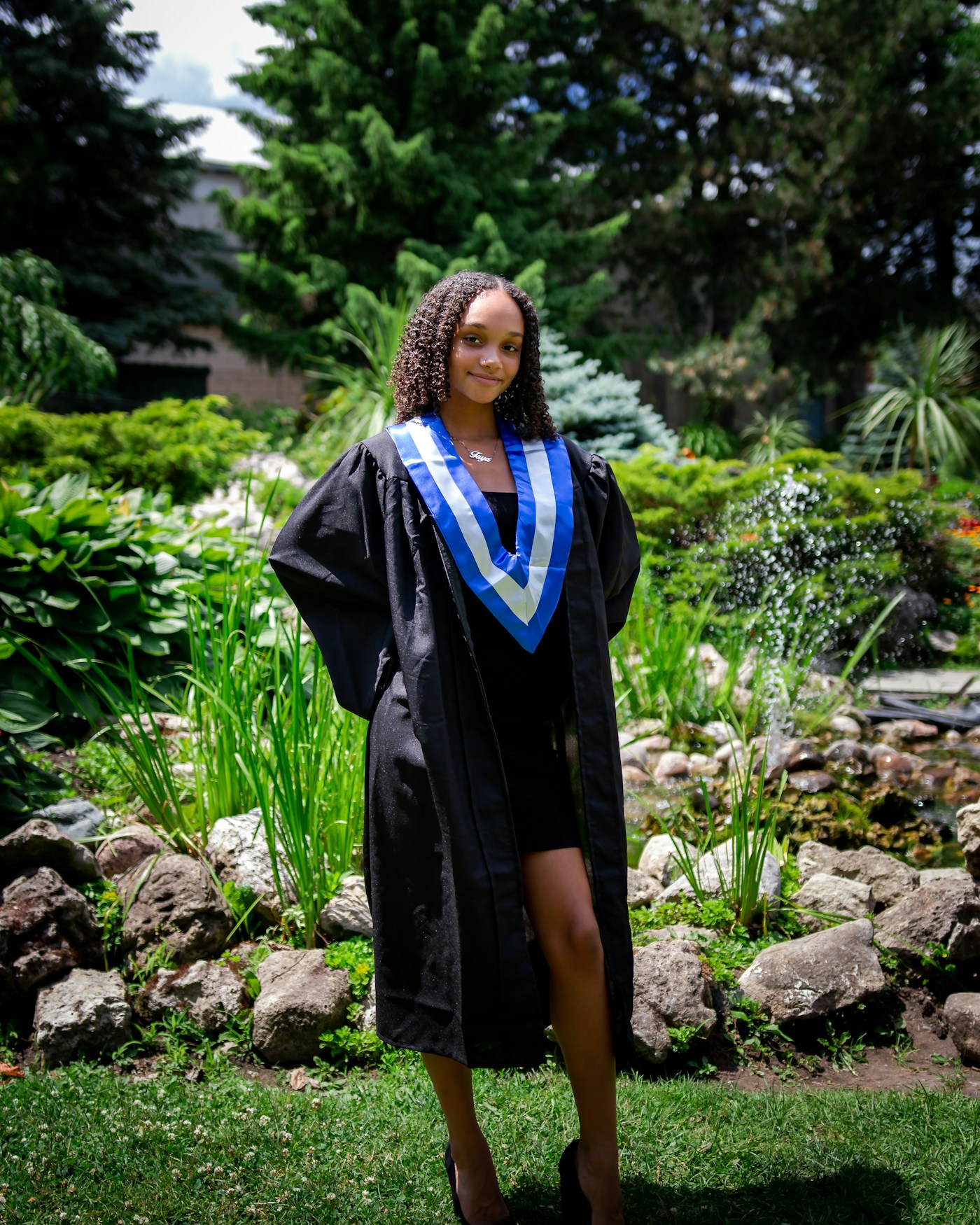 A graduate of the ISO Ambassadors programme standing in cap and gown in a Kampala garden.