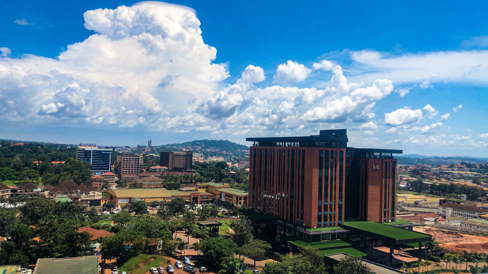 The Kampala skyline with a modern commercial tower under a bright sky.